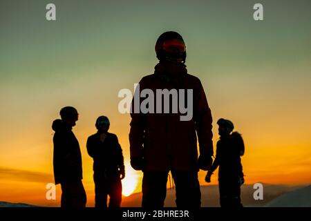 Vier Personen in Skianzügen, Schutzbrillen und Helmen, die gegen den Sonnenuntergang schillerten. Stockfoto