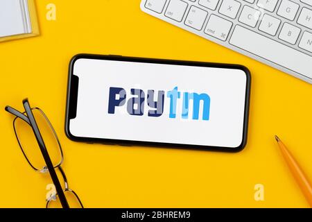 Ein Smartphone mit dem PayTM-Logo liegt auf einem gelben Hintergrund zusammen mit Tastatur, Brille, Stift und Buch (nur für redaktionelle Verwendung). Stockfoto