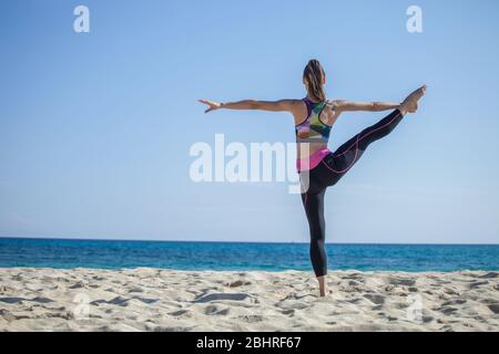 Rückansicht der Frau, die auf einem Sandstrand steht und Yoga macht. Stockfoto