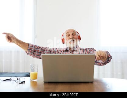 Porträt eines alten älteren Mannes mit Kopfhörer, der Musik auf einem Laptop zu Hause hört Stockfoto