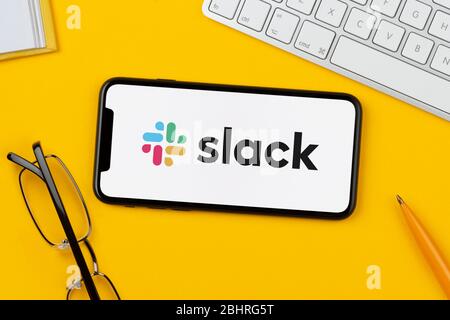 Ein Smartphone mit dem Slack-Logo liegt auf einem gelben Hintergrund zusammen mit Tastatur, Brille, Stift und Buch (nur für redaktionelle Verwendung). Stockfoto