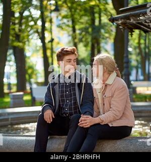 Liebhaber Junge und Mädchen schauen sich gegenseitig an, sitzen im Park in der Nähe des Brunnens im Herbst. Freundin und Freund sind im Gespräch Konzept der Liebe und Stockfoto