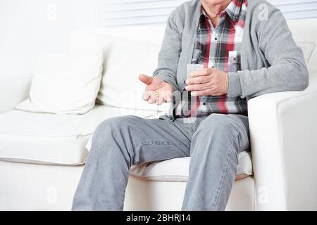 Senior schluckt Tablette mit Wasser im Wohnzimmer auf dem Sofa Stockfoto