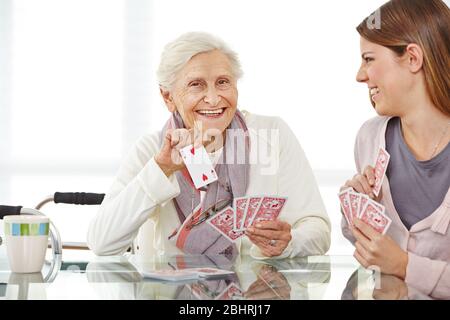 Junge Frau spielt Karten mit einer glücklichen älteren Frau in einem Altersheim Stockfoto