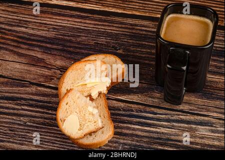 Frischer Weizentoast mit Butter und einem Keramikbecher mit Kaffee mit Milch auf Holzgrund. Nahaufnahme Stockfoto