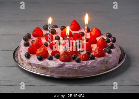 Hausgemachtes Geburtstagskäsekuchen mit Beeren und Geburtstagskerzen. Käsekuchen mit Erdbeere, Heidelbeere und Himbeere auf grauem Holzhintergrund. Stockfoto