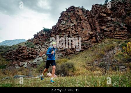 Sportler läuft hoch in den Bergen zwischen den Felsen. Bärtiger Typ joggt in den Bergen. Trailrunning Stockfoto