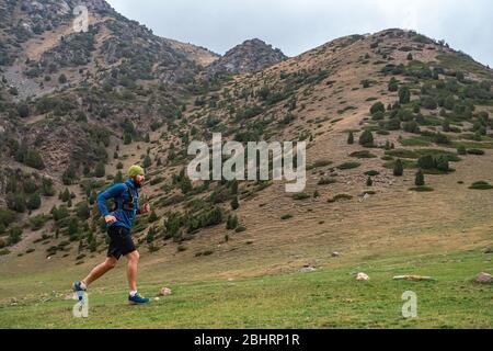 Sportler läuft hoch in den Bergen zwischen den Felsen. Bärtiger Typ joggt in den Bergen. Trailrunning Stockfoto