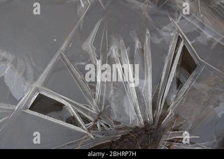 Nahaufnahme filigraner Eisformen und Nadeln auf einem kleinen gefrorenen Bach, mit etwas Pflanzenmasse. Stockfoto