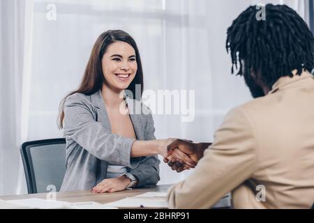 Selektiver Fokus des Mitarbeiters lächelnd und Händeschütteln mit afroamerikanischen Recruiter beim Vorstellungsgespräch im Büro Stockfoto