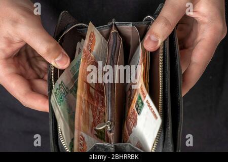 Ein Mann mit einer schwarzen Brieftasche voller russisches Geld. In einer schwarzen Brieftasche, Banknoten sind meist 5,000 Rubel pro Stück. Gehalt und Rente erhöht, Leistungen Stockfoto