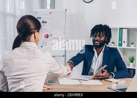 Selektiver Fokus von Mitarbeitern und afroamerikanischen Recruittern, die einander angucksen und sich die Hände am Tisch schütteln Stockfoto