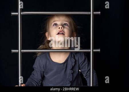 Ein kleines Mädchen in einer Maske klettert die Treppe. Bewegung zum Erfolg nach oben. Schaut mit der Hoffnung ein, dass Quarantäne zu Hause Selbstisolierung, Isolation beenden wird. Stockfoto