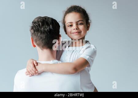 Rückansicht von Pflegevater umarmen glücklich angenommen afroamerikanischen Tochter isoliert auf weiß Stockfoto