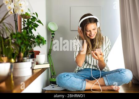 Glückliche Single Frau comunating und Musik auf dem Schreibtisch neben den Pflanzen und hellen Fenster hören, Arbeit von zu Hause, zu Hause bleiben. Stockfoto