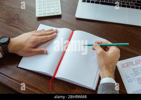 Teilansicht des Geschäftsmannes, der in Notebook in der Nähe Laptop und Rechner am Tisch im Büro schreibt Stockfoto