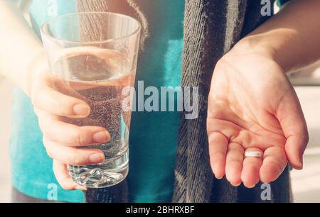 Nahaufnahme eines runden weißen Pille in junger weiblicher Hand. Frau nimmt Medikamente mit Glas Wasser. Tägliche Norm von Vitaminen, wirksame Medikamente Stockfoto
