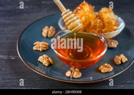 Bild von Honig tropft aus Honig Dipper in Glasschüssel. Dicker Honig, der aus dem hölzernen Honiglöffel taucht, Nahaufnahme. Draufsicht auf Honigtaupfer, Honig Stockfoto