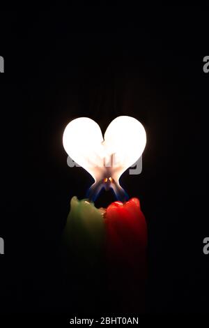 Zwei farbige brennende Kerzen mit einer Flamme in Form eines Herzens auf schwarzem Hintergrund Stockfoto