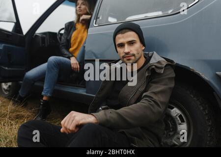 Mann in der schwarzen Hut sitzt in der Nähe seines Autos Stockfoto