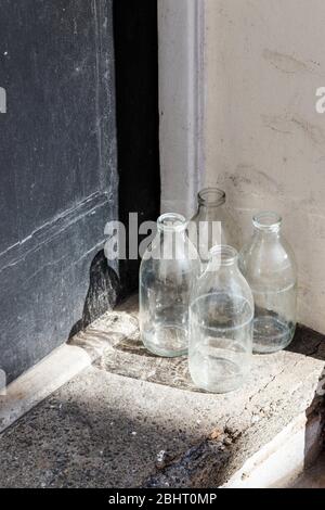 Vier leere Glasmilchflaschen warten vor der Haustür eines Wohnhauses auf die Abholung Stockfoto