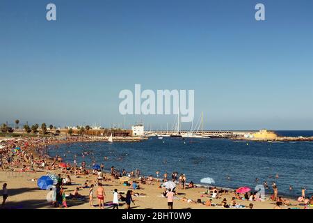 Blick auf viele Menschen, die sich auf Sand legen, sich am berühmten Strand 'La Barceloneta' in Barcelona sonnen. Es ist ein sonniger Sommertag Stockfoto