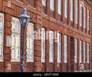 Antike Laterne vor einem großen Haus mit roter Ziegelmauer und vielen Fenstern Stockfoto