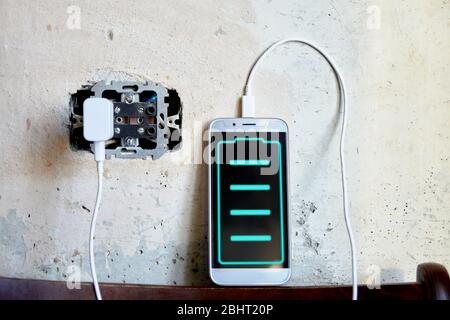 Telefon lädt vor dem Hintergrund einer Betonwand in einer Steckdose. Füllstandsanzeige auf dem Bildschirm Stockfoto