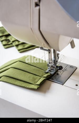 Nahaufnahme auf einem selbstgemachten wiederverwendbaren Tuch Gesichtsmaske aus grünem Baumwollgewebe, die auf einer Nähmaschine genäht wird. Stockfoto