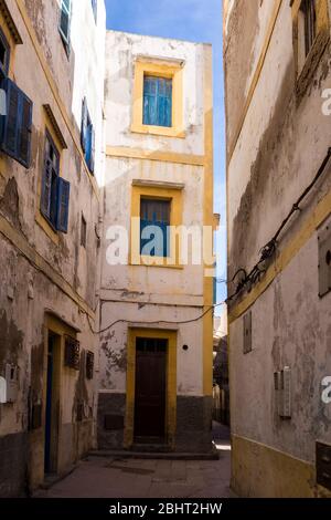 Schmale Straße mit Häusern mit kleinen Fenstern und blauen Fensterläden. Traditionelle weiße Fassade. Altstadt (Medina) von Essaouira, Marokko. Stockfoto