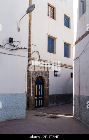 Schmale Straße mit Häusern mit kleinen Fenstern und blauen Fensterläden. Traditionelle weiße Fassade. Altstadt (Medina) von Essaouira, Marokko. Stockfoto