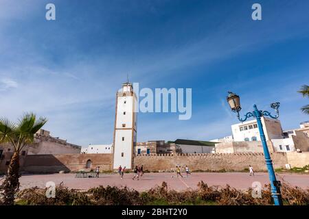 Fußball spielen in Stadtmauern und Moschee Ben Youssef Minarett, Essaouira, Marokko Stockfoto