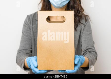 Lieferung Lebensmittelservice während der Quarantäne wegen Coronavirus Ausbruch. Frau mit einer Schachtel in medizinischen Handschuhen und Schutzmaske. Stockfoto