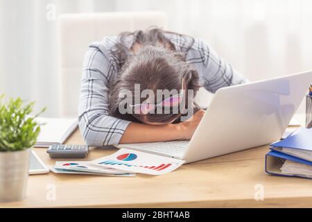 Frau schlief auf ihrem Schreibtisch mit Geschäftsgraphen und einem Notizbuch vor ihr ein. Stockfoto
