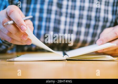 Geschäftsmann in karierten Hemd halten Stift und Umblättern von Notizbuch in Büro Hände Fokus Stockfoto