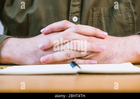 Mann, der die Finger während des Meetings auf dem Schreibtisch hält, konzentriert sich auf die Hände Stockfoto