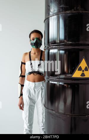 Futuristische afroamerikanische Frau in Sicherheitsmaske in der Nähe radioaktiver Abfälle Fässer auf weiß isoliert Stockfoto