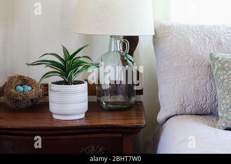 Bauernhaus Stil Schlafzimmer mit Topfweiß Juwel, Zimmerpflanze auf einem antiken Waschtisch durch ein bequemes Bett. Hausgemachte Lampe auf der Kommode. Stockfoto