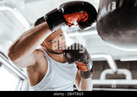 Selektiver Fokus des gutaussehenden Sportlers im Boxhandschuh-Training mit Boxsack Stockfoto