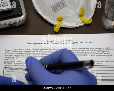 Eine gummihandschuppte Hand ist im Begriff, ein Paycheck Protection Program PPP-Darlehen Formular auszufüllen, das von der US-Regierung Small Business Administration zur Verfügung gestellt wird. Stockfoto