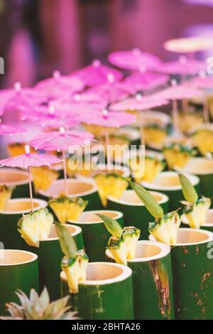 Bambus Tassen exotischer Cocktail-Drinks mit bunten Regenschirmen und Strohhalmen. Cocktail in der ersten Zeile in der Mitte ist im Fokus der Kamera. Dunkle Bereiche und Rücken Stockfoto