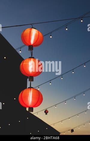 Reise- und Urlaubskonzept. Rot hängende chinesische Lampen und Girlanden in blauen und klaren Sonnenuntergang Himmel während ruhigen und warmen Spätsommerabend in Thailand. Stockfoto