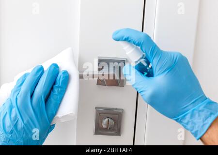 Hände in Schutzhandschuhe - einer hält die Spritze mit einem Antiseptikum, der andere - wischen den Türgriff mit einem Tuch angefeuchtet mit einem Desinfektionsmittel Stockfoto