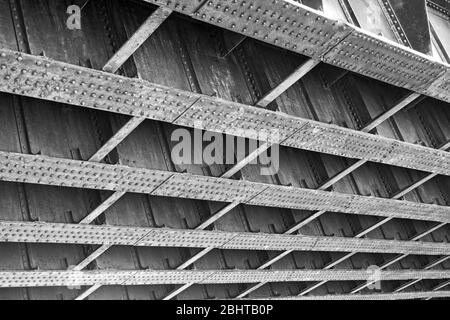 Unterseite einer alten stillgehaltener Eisenbahnbrücke, die Details von Stahlplatten und Nieten zeigt, die die Konstruktion zusammenhalten. Stockfoto