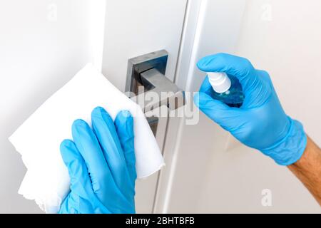 Hände in Schutzhandschuhe - einer hält die Spritze mit einem Antiseptikum, der andere - wischen den Türgriff mit einem Tuch angefeuchtet mit einem Desinfektionsmittel Stockfoto