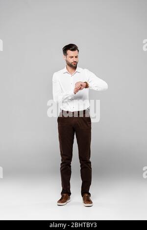 Gutaussehende Geschäftsmann in weißem Hemd Blick auf Uhr auf grau Stockfoto