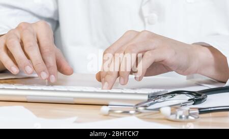 Hände des Doktors, der auf Tastatur des Computers mit Stethoskop in einer Klinik, nah oben schreibt. Stockfoto