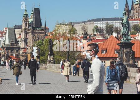 Prag, Tschechische Republik - 23. April 2020: Menschen, die medizinische Gesichtsmasken auf der Karlsbrücke tragen. Altstadt im Hintergrund. Stadtzentrum während der Coronavirus-Pandemie. COVID-19-Krise. Horizontales Foto. Stockfoto