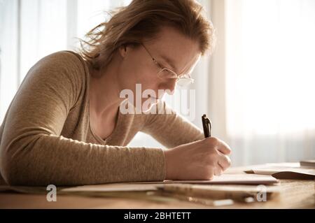 Junge Frau konzentrierte sich auf das Schreiben Hausaufgaben während des Studiums zu Hause Stockfoto