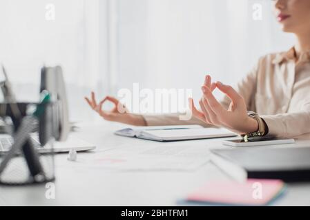 Ansicht der Geschäftsfrau, die mit Gyan Mudra am Arbeitsplatz meditiert, mit Notizblock Stockfoto